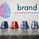 Four modern chairs (three blue, one red) are lined up against a wall adorned with a large colorful fingerprint graphic and the word "brand" beside it. Below "brand," the text reads: "Build your brand and protect it." The wooden floor complements this stylish take on branding.